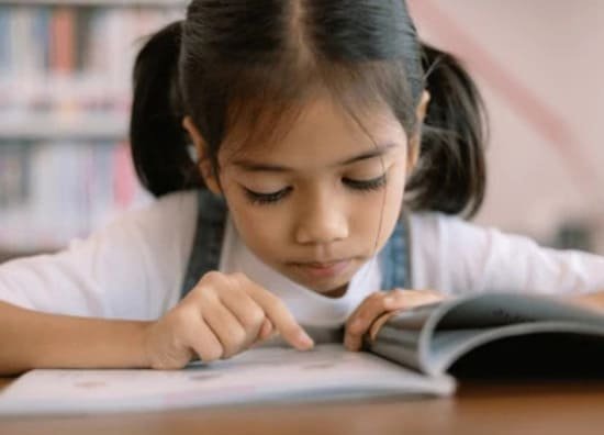 Elementary girl reading a book, focused on text during her English lesson.