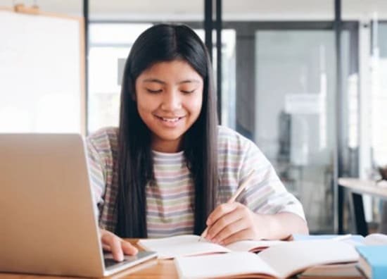 Girl smiles while studying online lesson with a laptop and notebook.