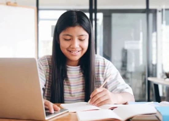 ノートパソコンとノートを使ってオンライン英語を学ぶ女の子
