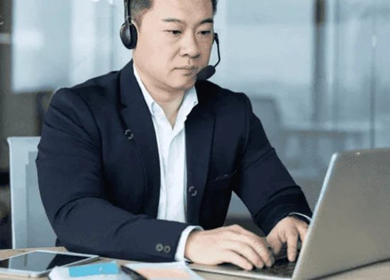 スーツ姿の男性がヘッドセットを着けて、オンラインでビジネス英語とコミュニケーションを学んでいる様子。
